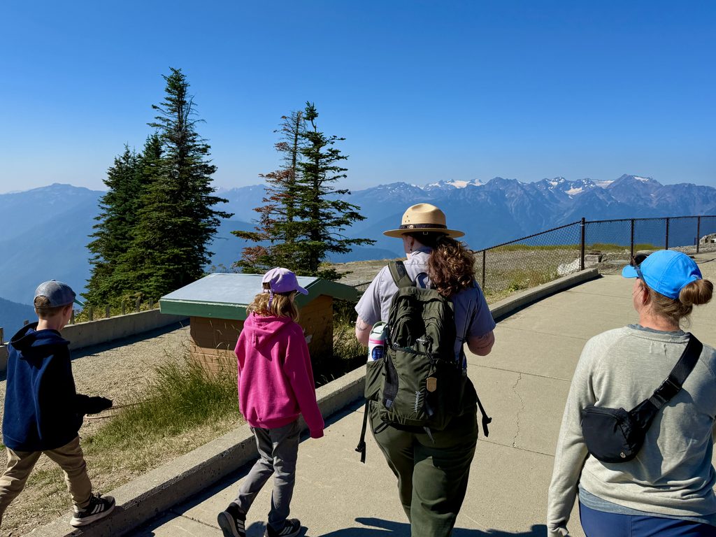 Walking the ridge with a ranger, snowy peaks ahead.